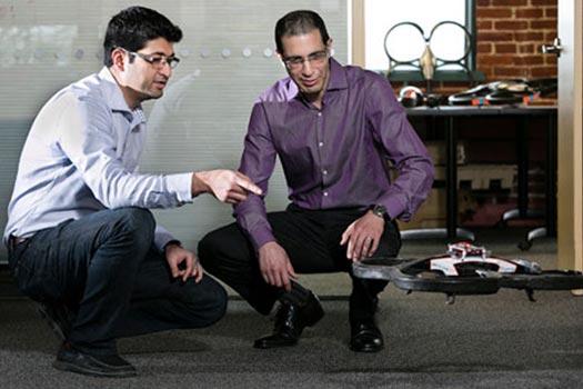 Two men squatting on the ground, interacting with a robot