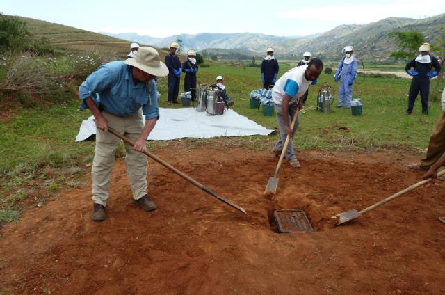 Two men install a mobile soak pit in the ground.
