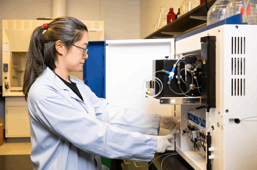A woman in a lab coat works with equipment in a lab.