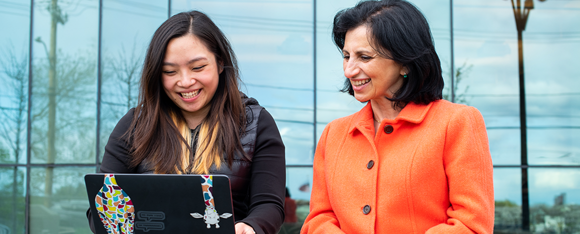 Two women work on a laptop outside the Joyce Cummings Center at Tufts University.