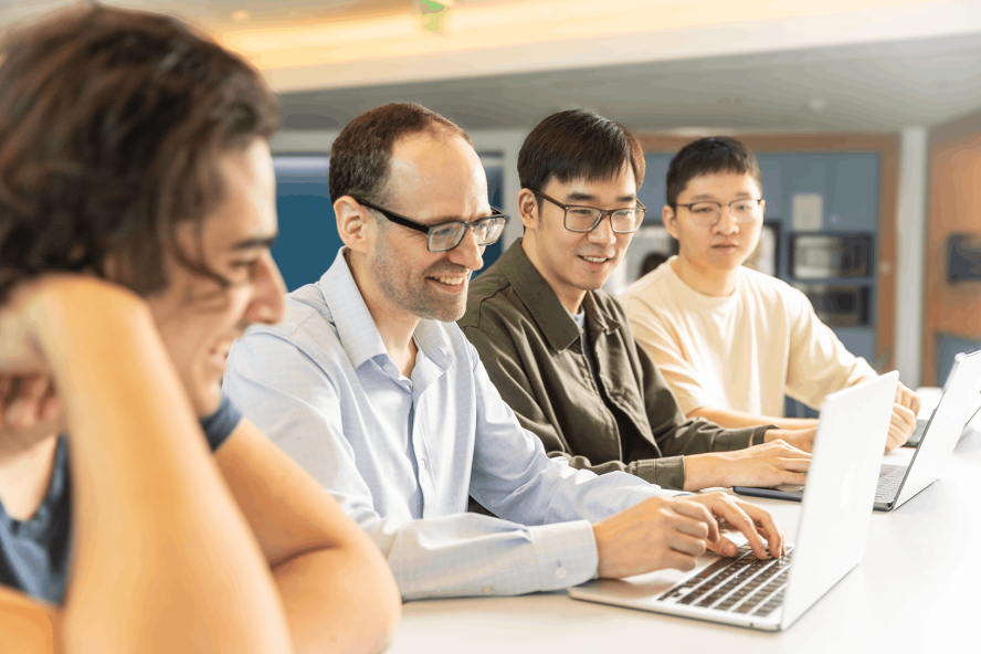 A professor with a laptop instructs three students.