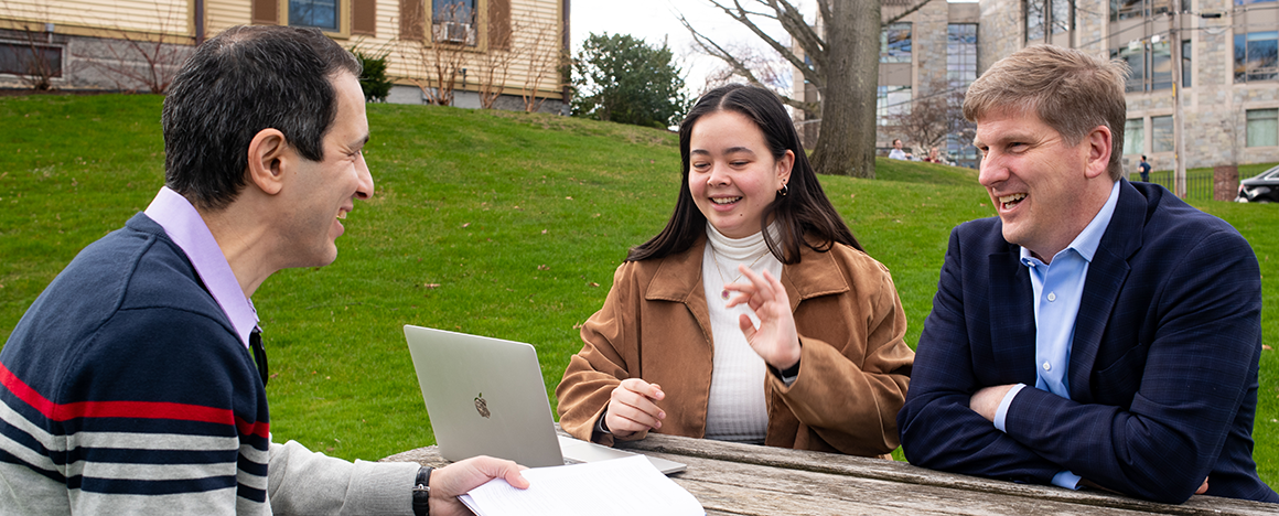 Professors Babak Moaveni and Eric Hines talking at a table with student Bridget Moynihan