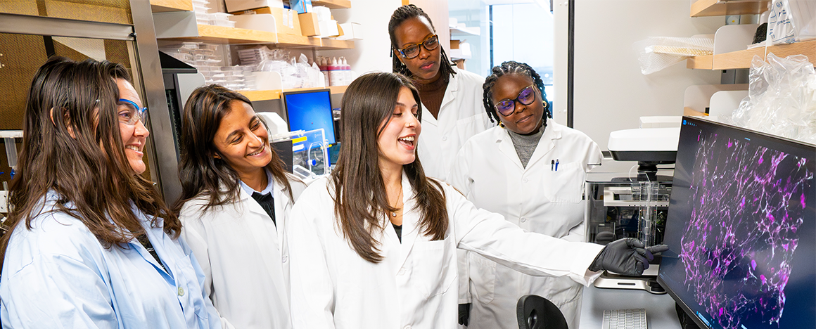 Left to right: Shelly Peyton, Maulee Sheth, Haylee Wagner, Ninette Irakoze, and Tianna Edwards look at a screen together in Shelly Peyton's lab. Haylee is gesturing towards the screen.