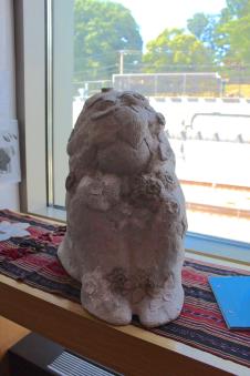 Grey sculpture that looks appears to look like a person hugging their knees