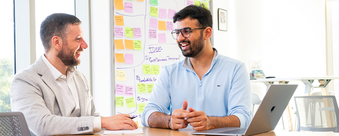 Smit Patel (right) talks with Filip Čučkov (left). Behind them is a white board covered in colorful sticky notes.