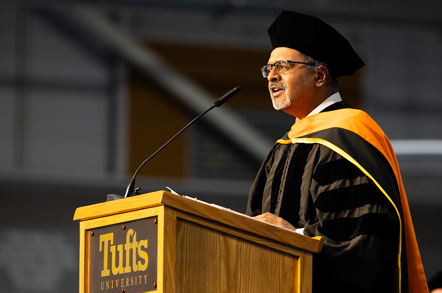 Dr. Arul Jayaraman in academic regalia delivering remarks at Tufts podium
