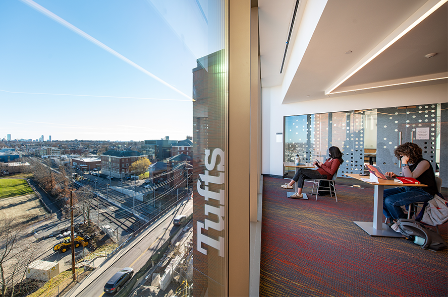 Students study in Joyce Cummings Center with the Boston skyline visible outside the window.