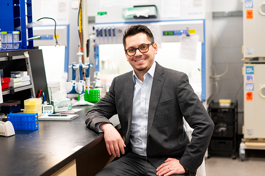 Juan Gnecco sitting at laboratory bench surrounded by lab equipment 