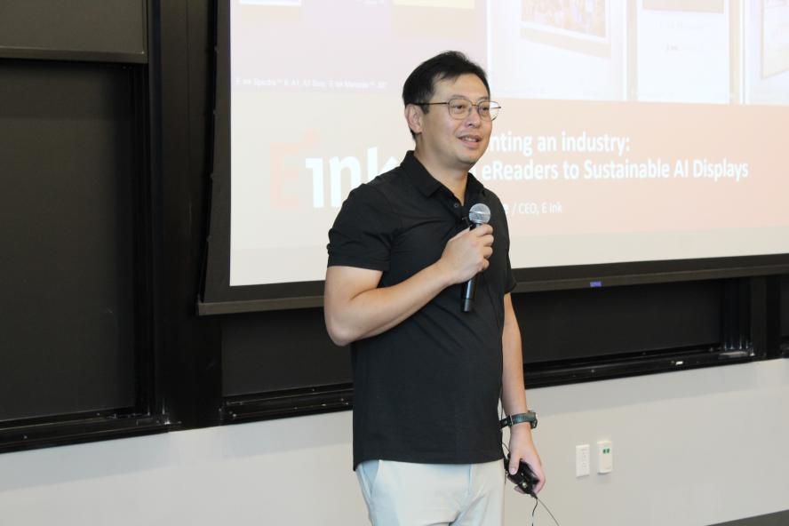 Johnson Lee holding up a microphone in front of a presentation in the background