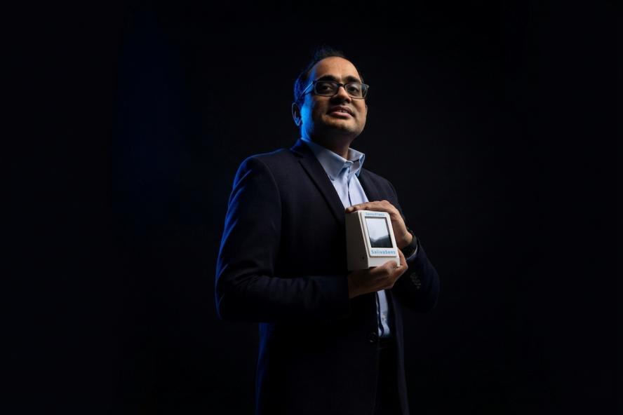 Sameer Sonkusale posing with small white device in front of a dark background