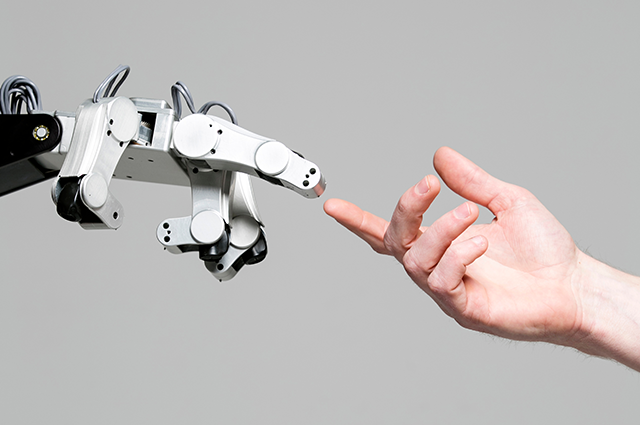 A robot hand and a white person's hand reach towards each other against a grey background.
