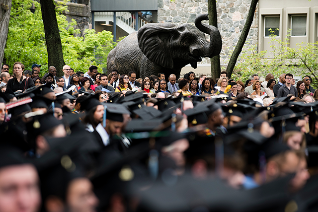 An elephant statue with many people in graduation hats sitting in front of it.