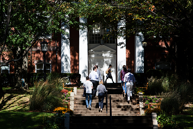 A shot of people walking into a building shaded by leafy trees