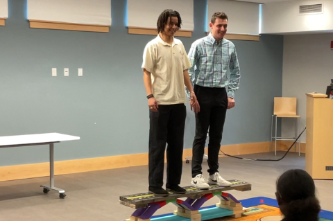 Sophomores in civil engineering Milo Kiddugavu and Ethan Kessler stand on top of a model bridge during a presentation at the Stoughton Public Library.