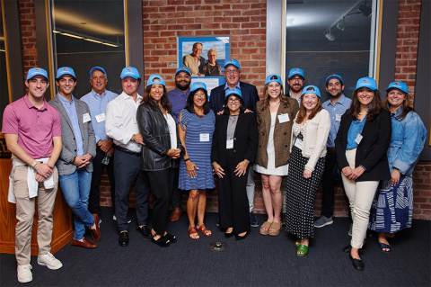 Members of the Haymon family wearing Tufts baseball caps, gathered in the Monte and Jane Haymon Boardroom.