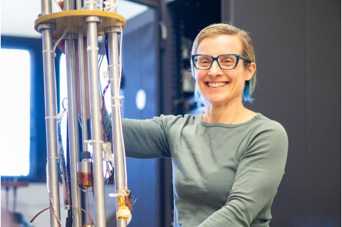 Woman smiles posing with large research laboratory device