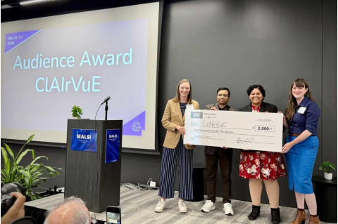 Four young adults posing in front of powerpoint presentation with large check award