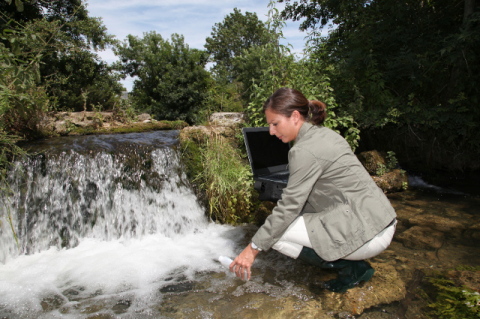 A woman collects a water sample from a waterfall.
