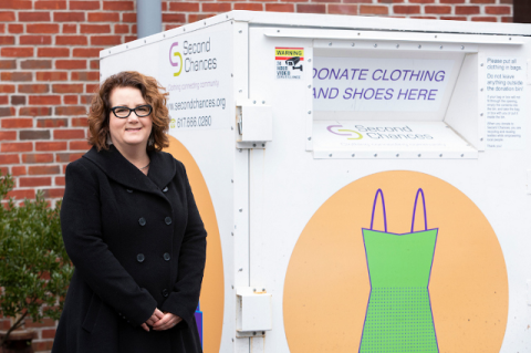 A woman stands in front of a large clothing donation box