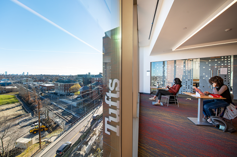 Students studying in the Joyce Cummings Center, overlooking the Medford campus and a view of the Boston skyline in the distance.
