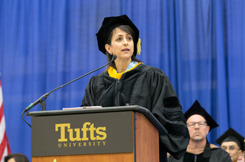 A white woman with brown hair stands at a Tufts podium in academic regalia