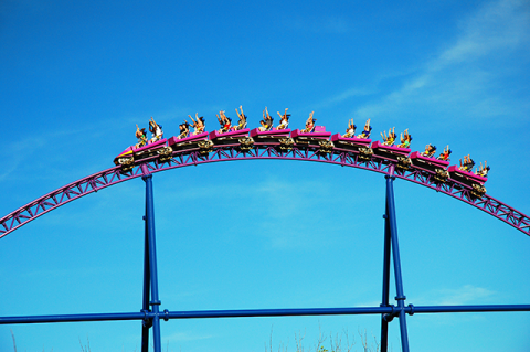 A roller coaster car full of people in the air against a blue sky