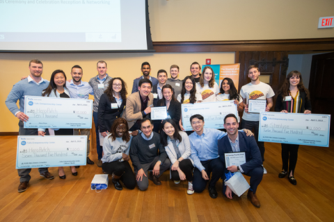 Winners from the $100k New Ventures Competition pose for a group photo with their large prop checks